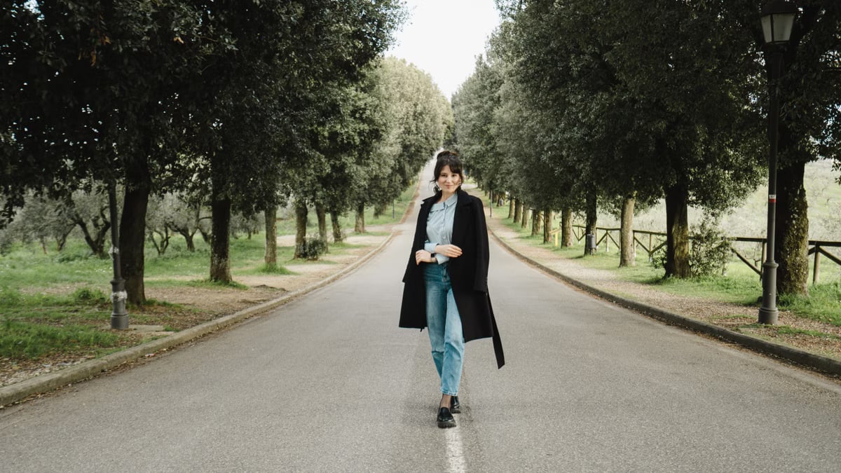 Stylish woman walking on a beautiful tree-lined road in the Tuscan countryside.